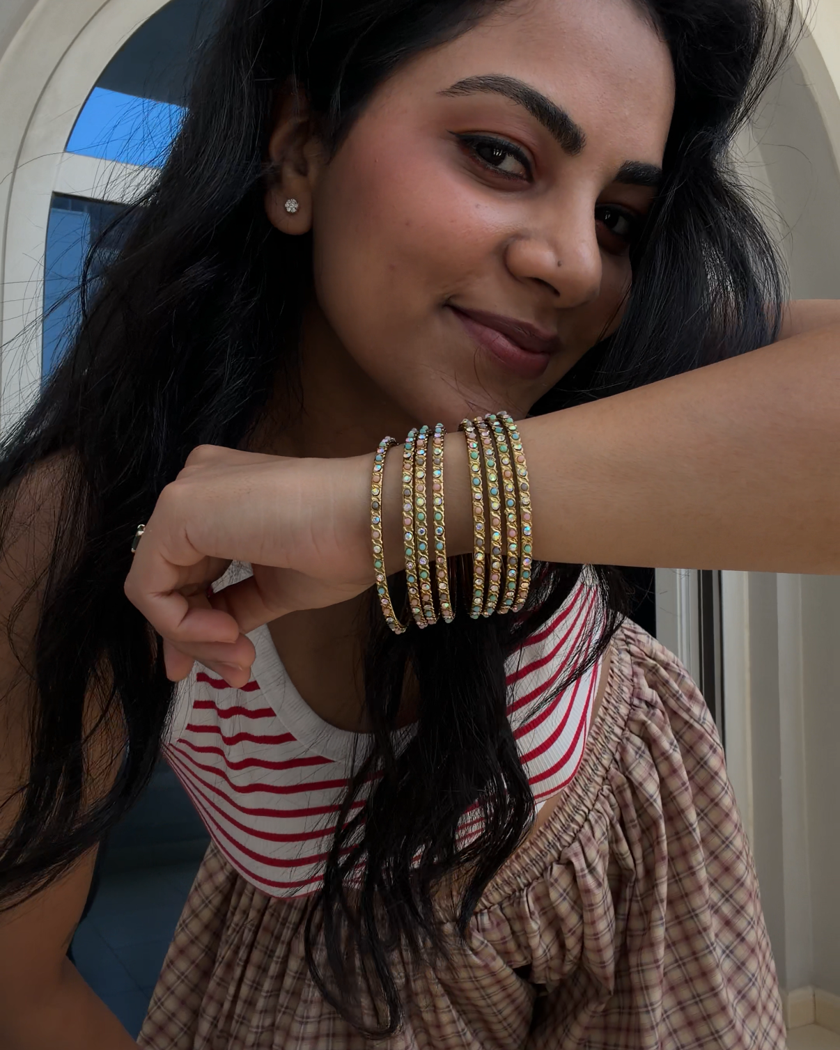 Indowestern Look. Accessorized with multiple gold bangles on her wrist, posed in front of a white arched doorway